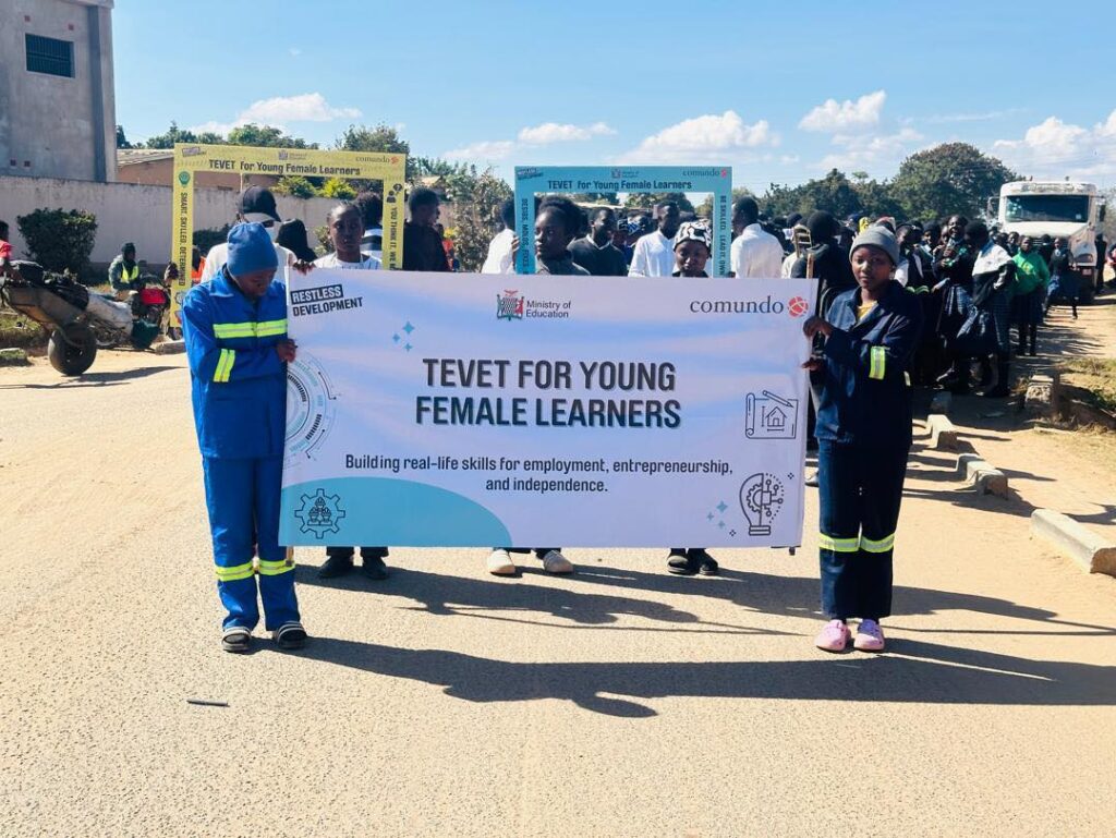 young people leading a march past, holding a TEVET for young female learners banner