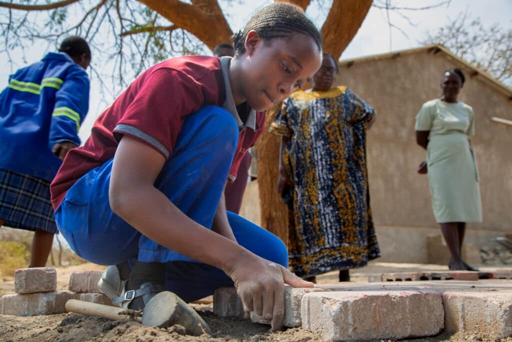 Pupil installing pavers with headteacher and others watching.
